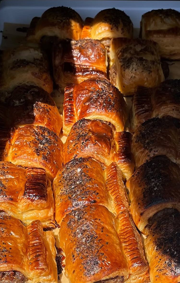 Golden-brown puff pastry sausage rolls topped with poppy seeds on a baking sheet.