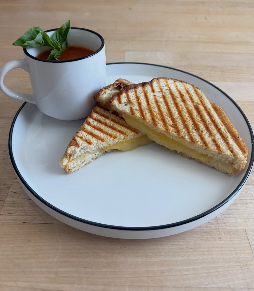 Grilled cheese sandwich and tomato soup with basil on a white plate.