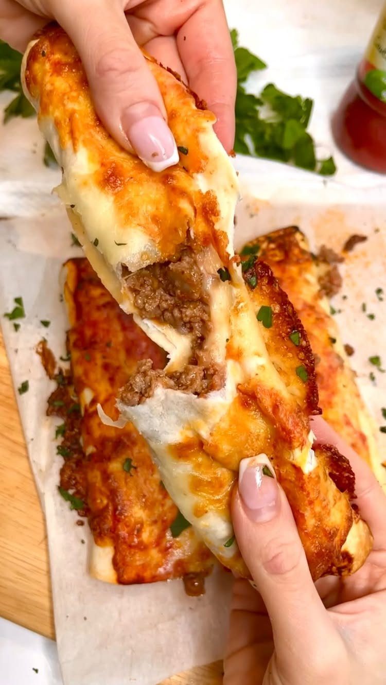 Cheesy baked tortilla rolls filled with ground meat being pulled apart by hands.