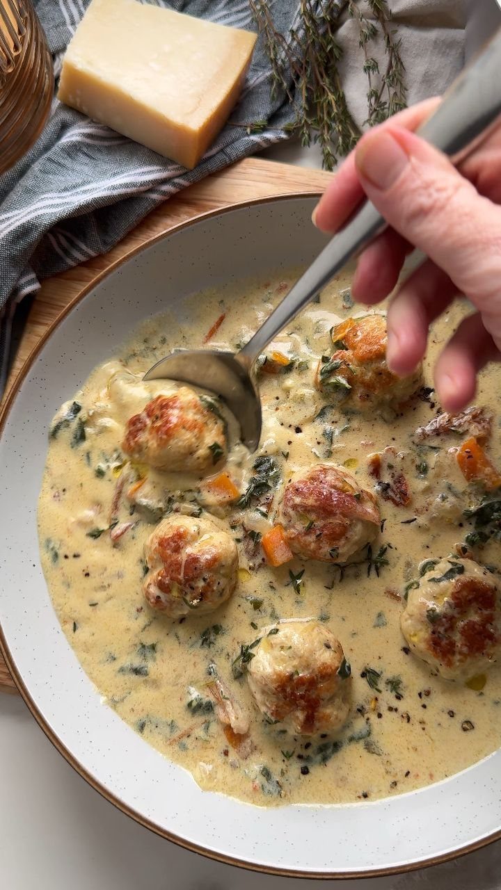 Meatballs in a creamy spinach and sun-dried tomato sauce in a white pan.