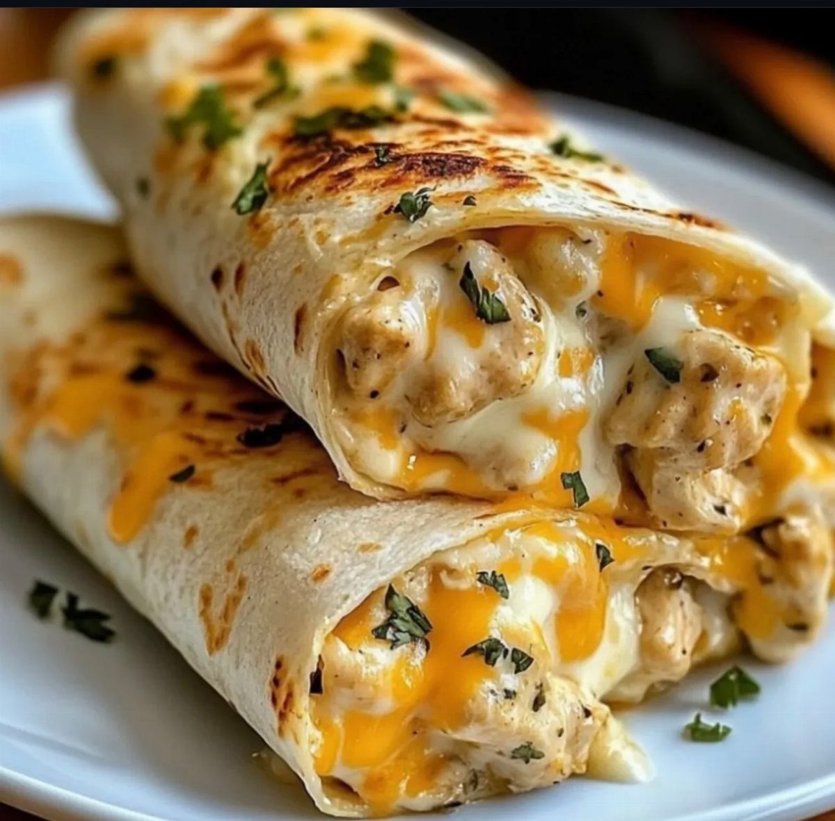 Grilled chicken burritos filled with melted cheese and herbs on a white plate