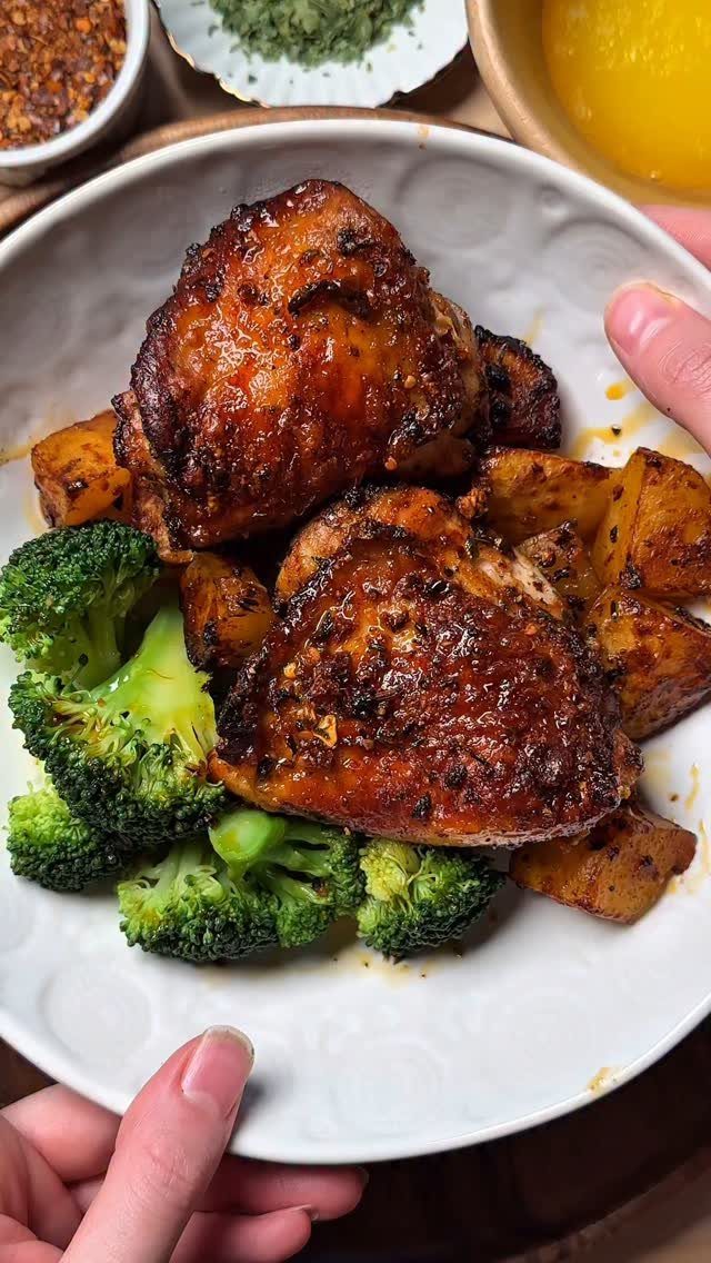 Glazed chicken thighs with roasted potatoes and broccoli on a white plate.