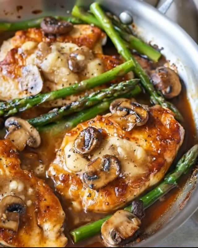 Seared chicken breasts with mushrooms and asparagus in a stainless steel skillet