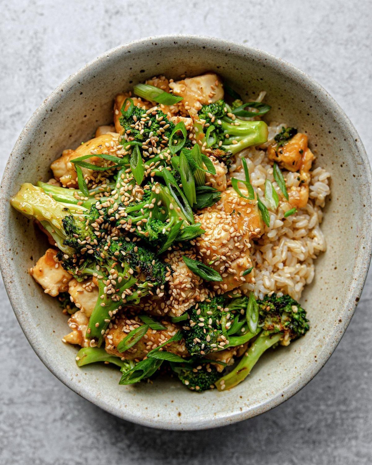 Sesame tofu and broccoli served over brown rice in a grey ceramic bowl.
