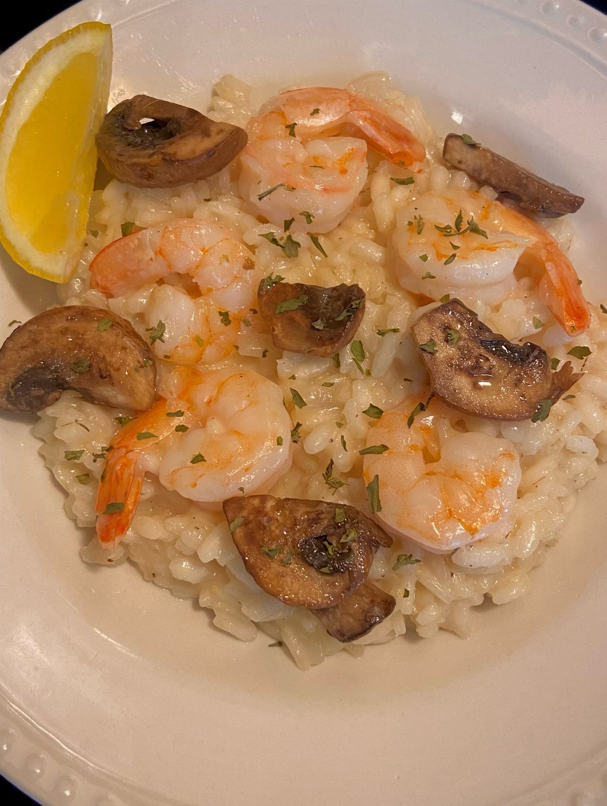 Creamy risotto topped with pink shrimp, sautéed mushrooms, and a lemon wedge.