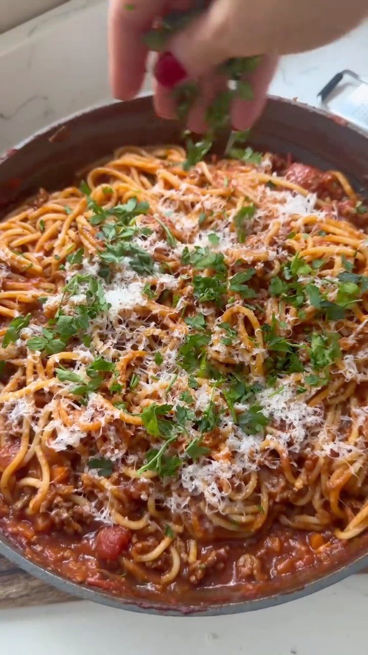 Spaghetti Bolognese in a pan topped with parmesan cheese and fresh parsley.