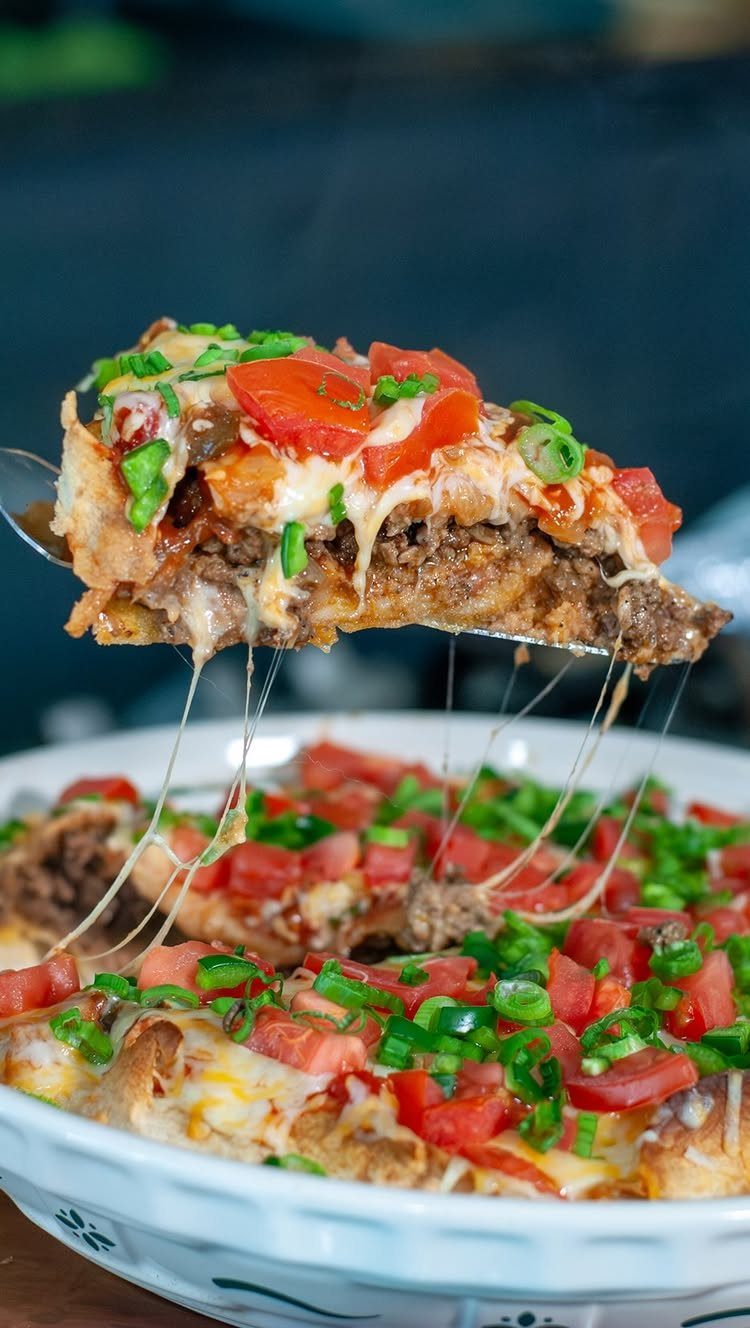 Taco pie slice with melted cheese, ground beef, tomatoes, and green onions.