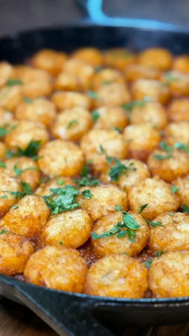 Tater tots with parsley in a black cast iron skillet over red sauce.