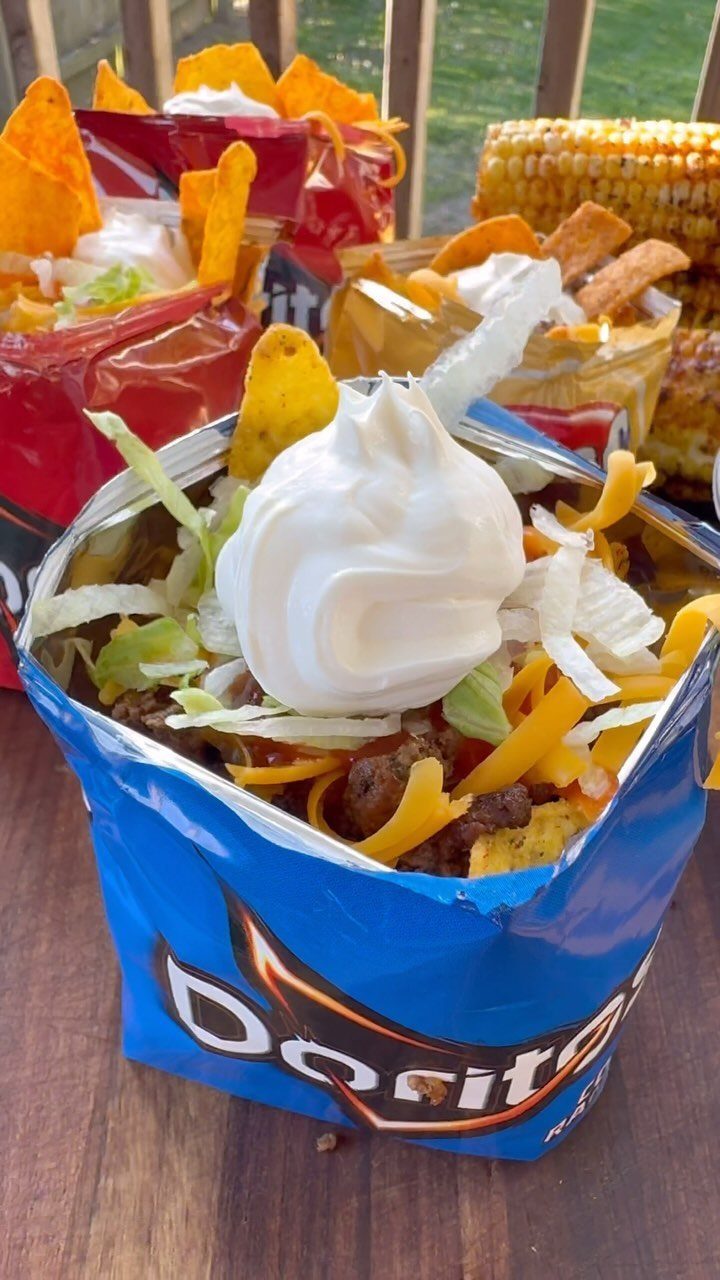 Taco ingredients served inside open Doritos chip bags topped with sour cream.