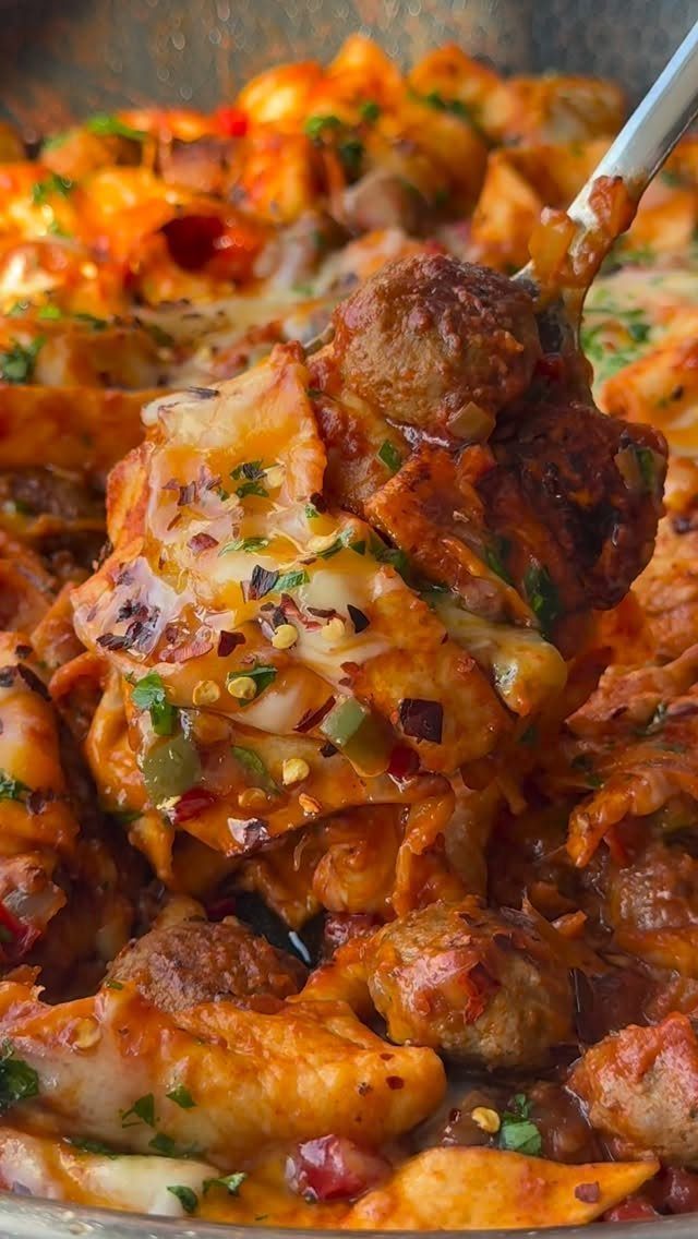 Cheesy pasta bake with meatballs and red sauce lifted by a silver spoon.