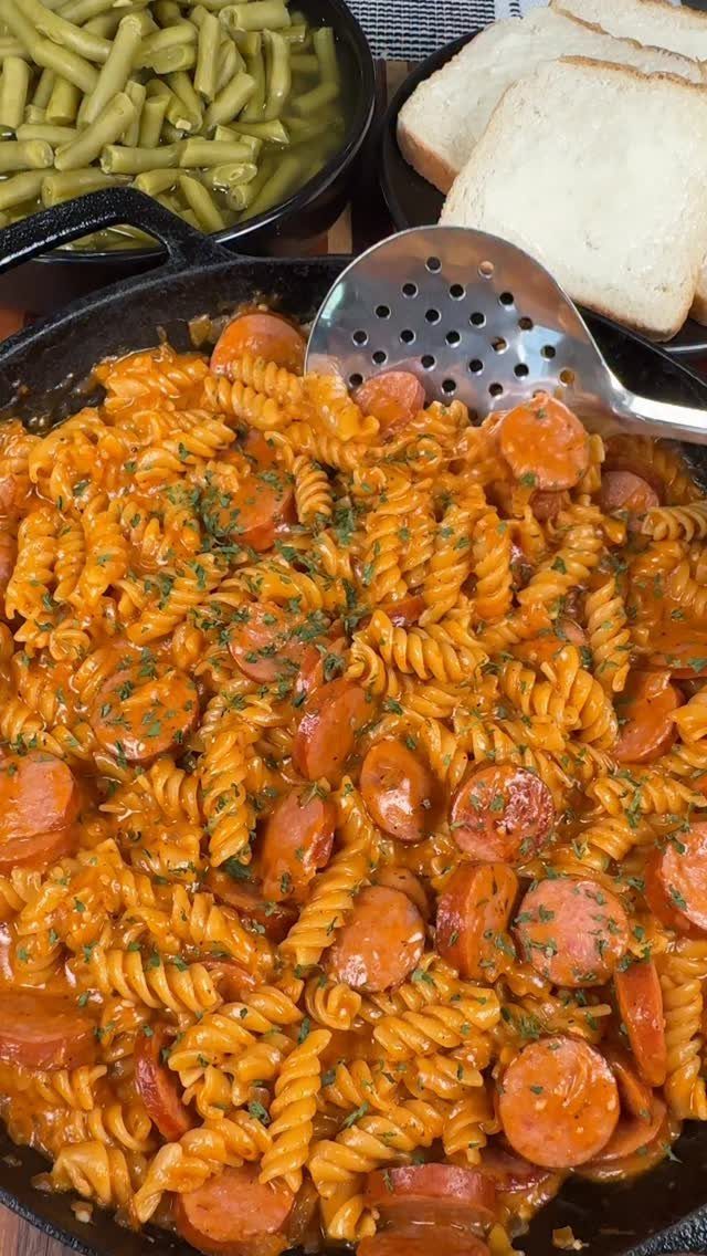 Rotini pasta and sliced sausage in orange sauce with green beans and bread.