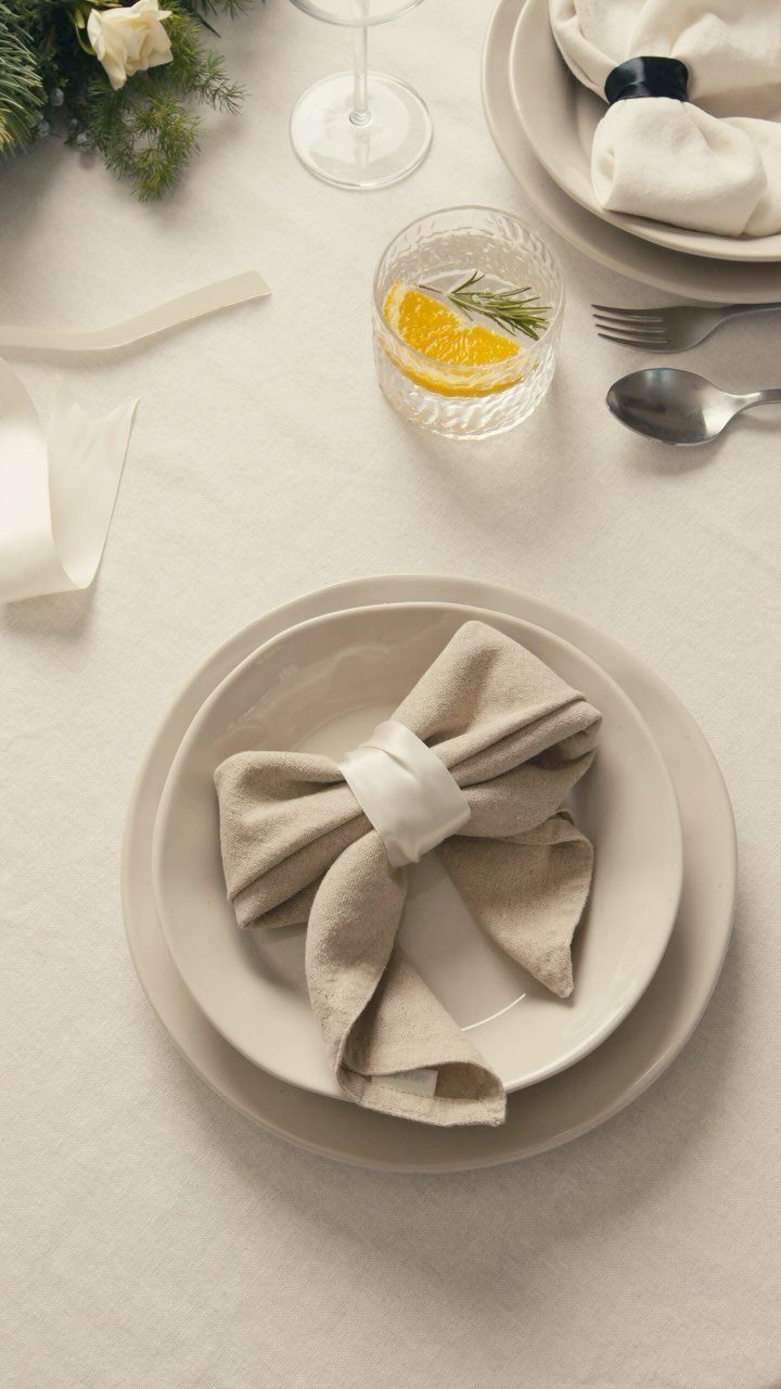 Beige linen napkin folded into a bowtie shape with a white ribbon tie.