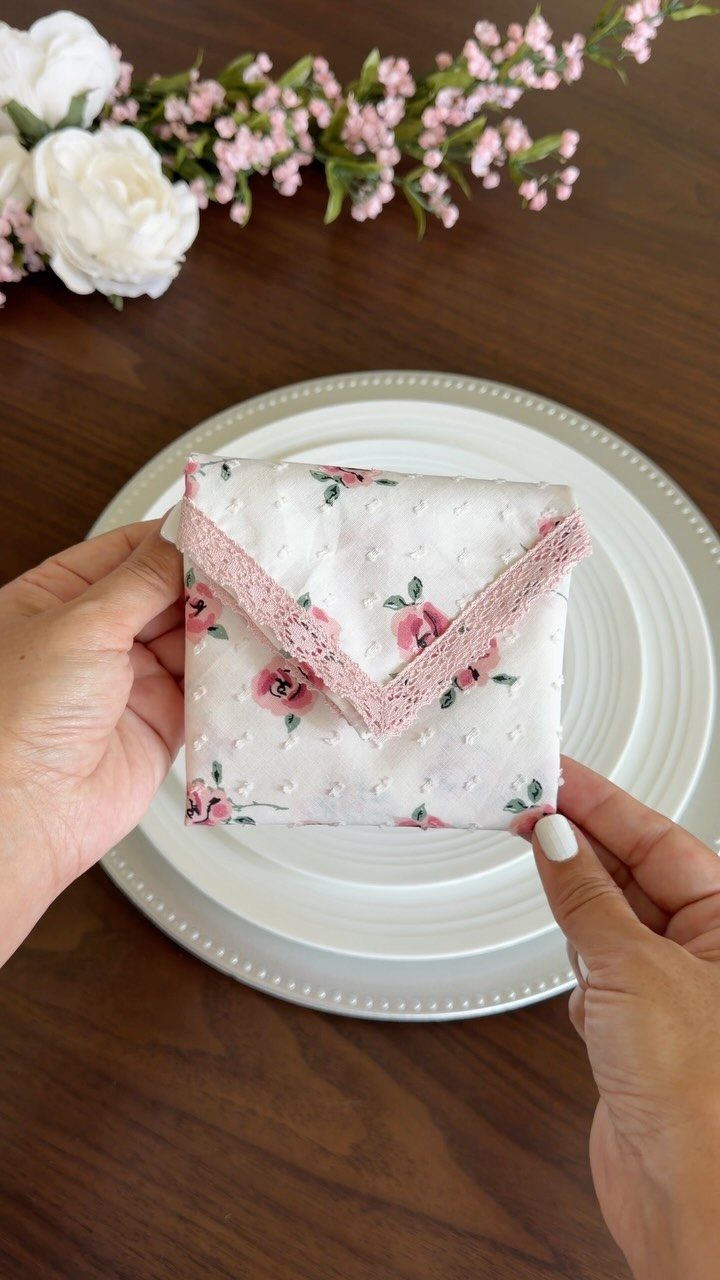 Floral white napkin folded into an envelope shape held over white dinner plates.