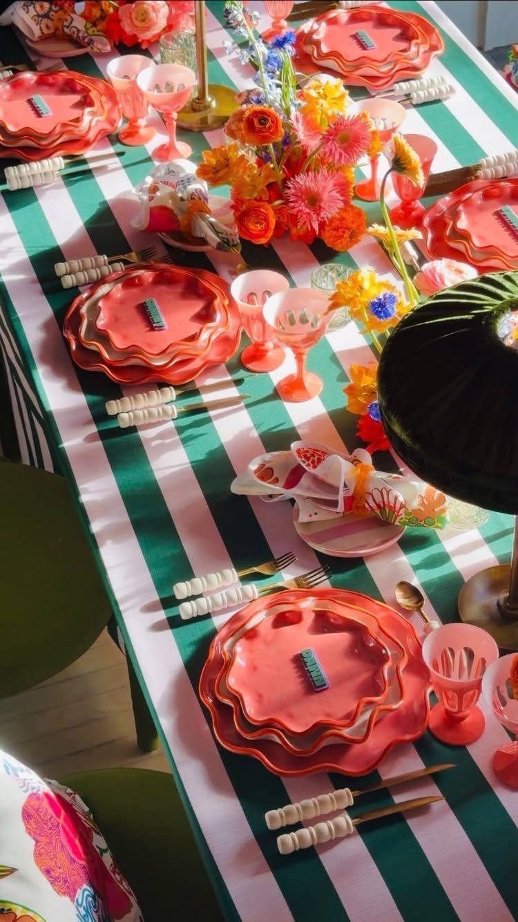 Vibrant table setting with red scalloped plates and orange flowers on striped tablecloth