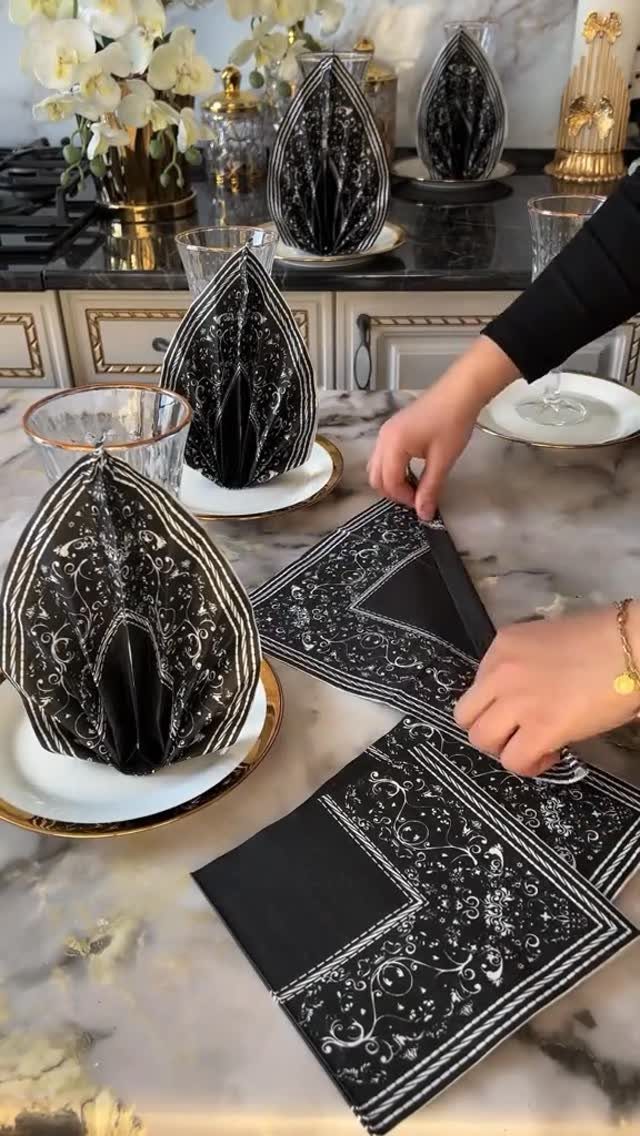 Hands arranging black patterned napkins on white gold-rimmed plates over a marble table.