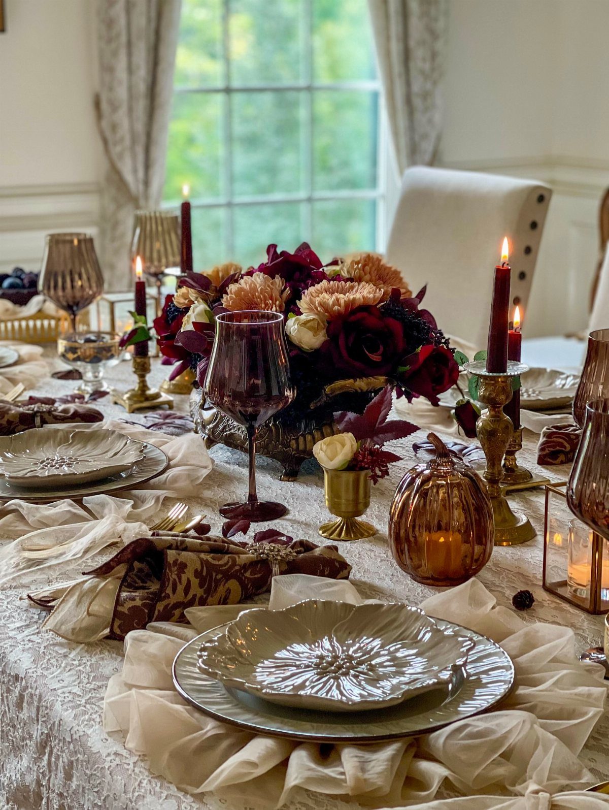 Elegant table setting with burgundy flowers, candles, and white textured plates on lace.