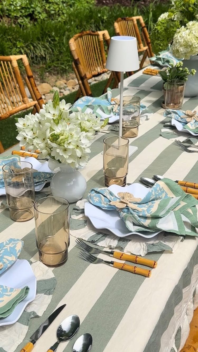 Outdoor table setting with striped tablecloth, bamboo cutlery, and white floral centerpieces.