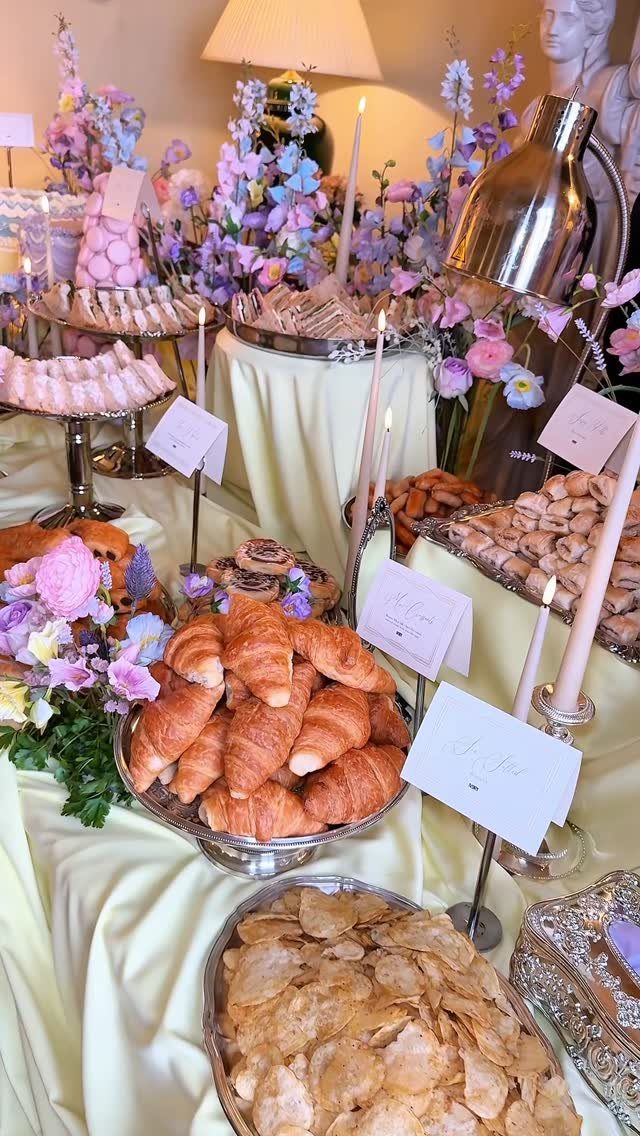 Buffet table with yellow linens, silver platters of pastries, and pastel floral arrangements.