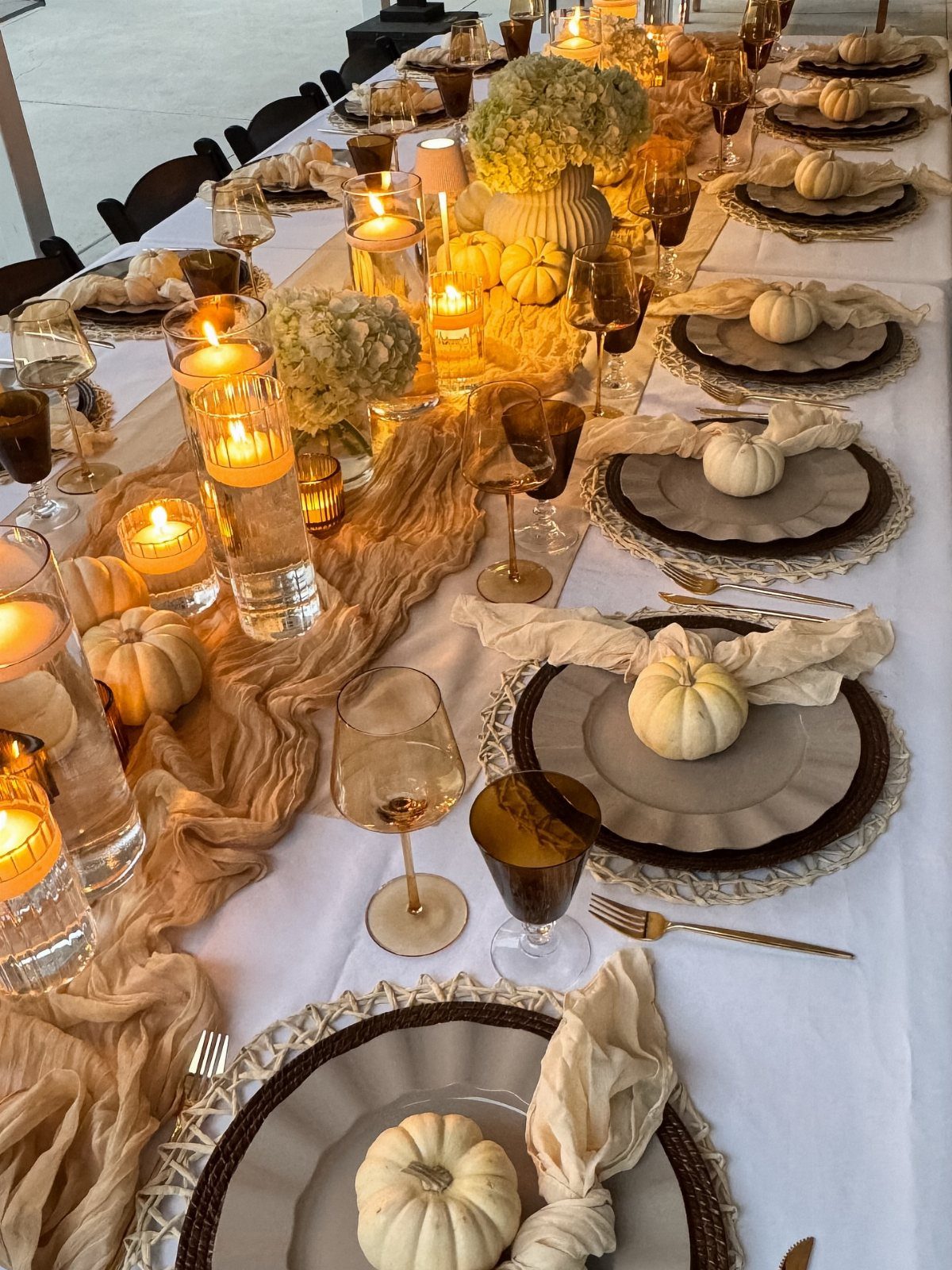 Beige table setting with white pumpkins, floating candles, and woven placemats on white linen.