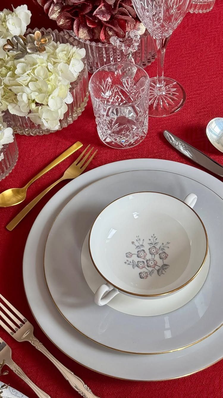White plates with gold rims and crystal glasses on a red tablecloth.