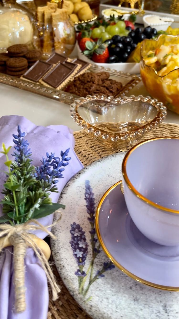 Purple teacup and saucer on a woven placemat with lavender and snacks.