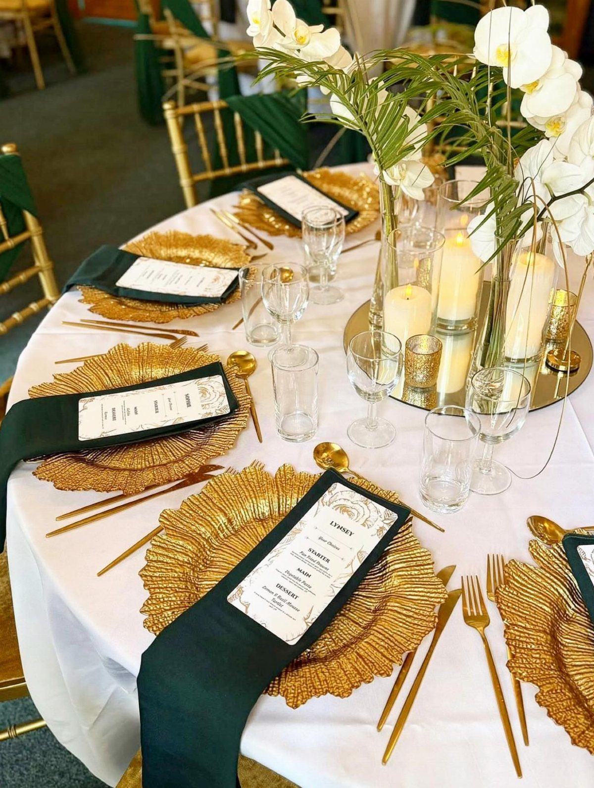 Gold charger plates on a white tablecloth with green napkins and white orchids.