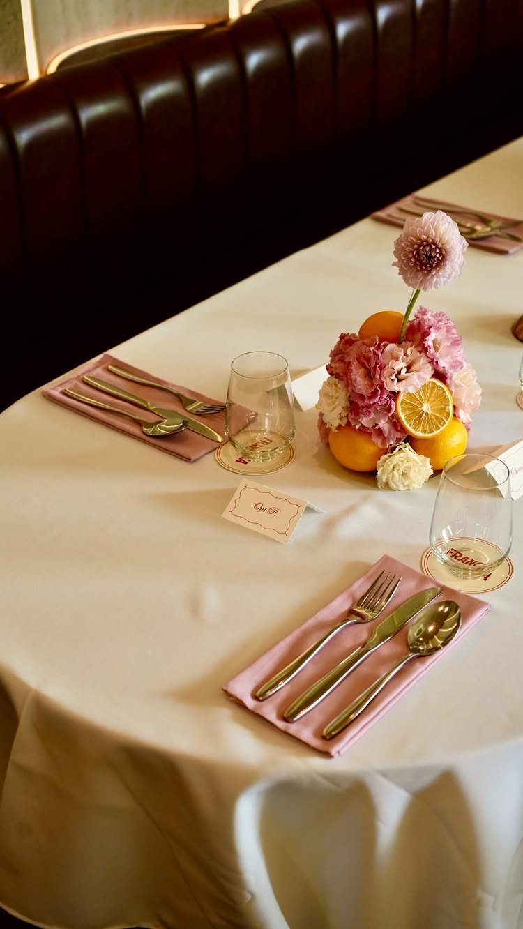White table setting with pink napkins, gold cutlery, and a small place card.