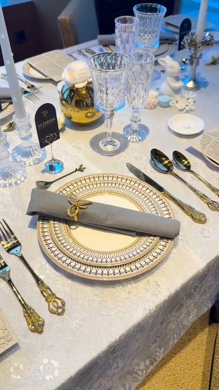 Formal table setting with gold-rimmed plates, ornate cutlery, and crystal glasses on lace.