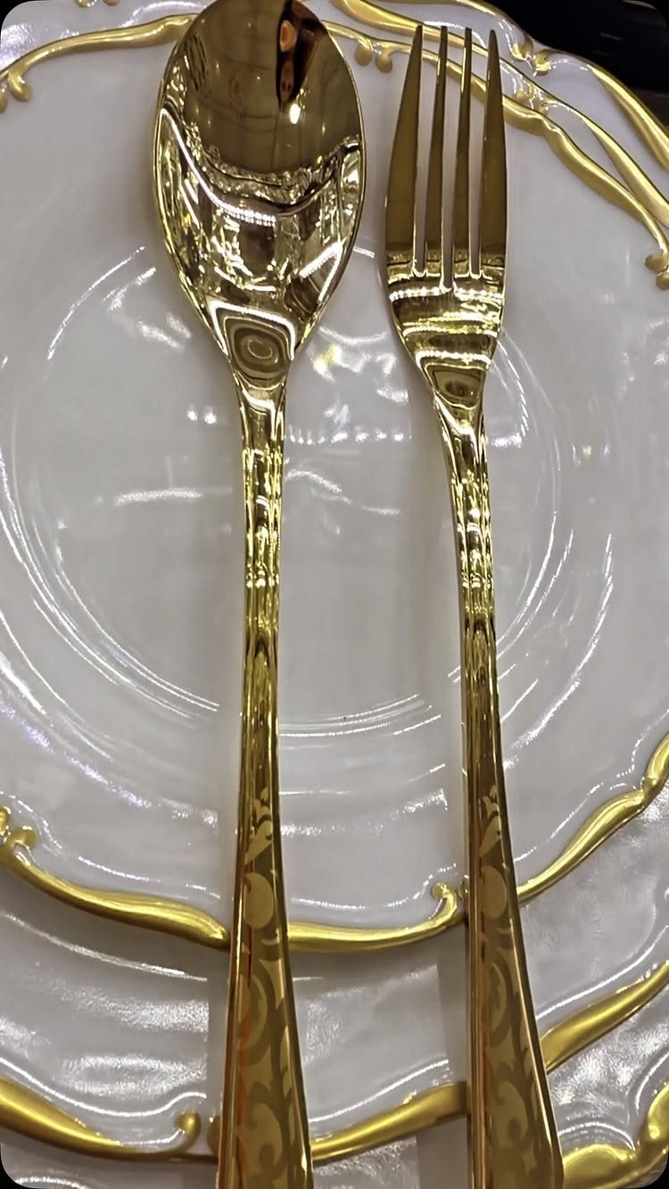 Gold spoon and fork on a white plate with gold ornate edges.