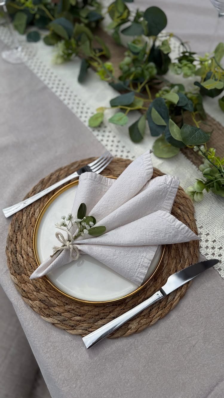 White gold-rimmed plate on a woven charger with a tied cloth napkin.