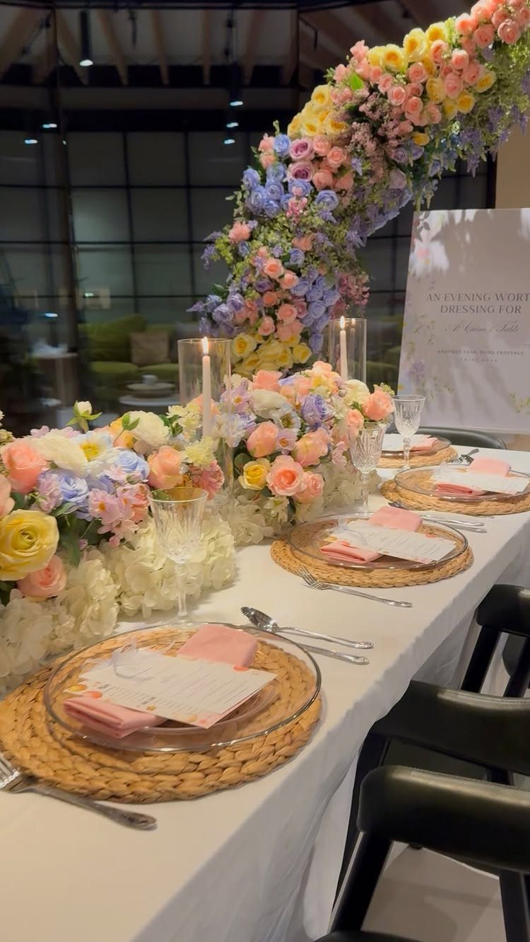Pastel floral table setting with woven chargers, pink napkins, and a flower arch.