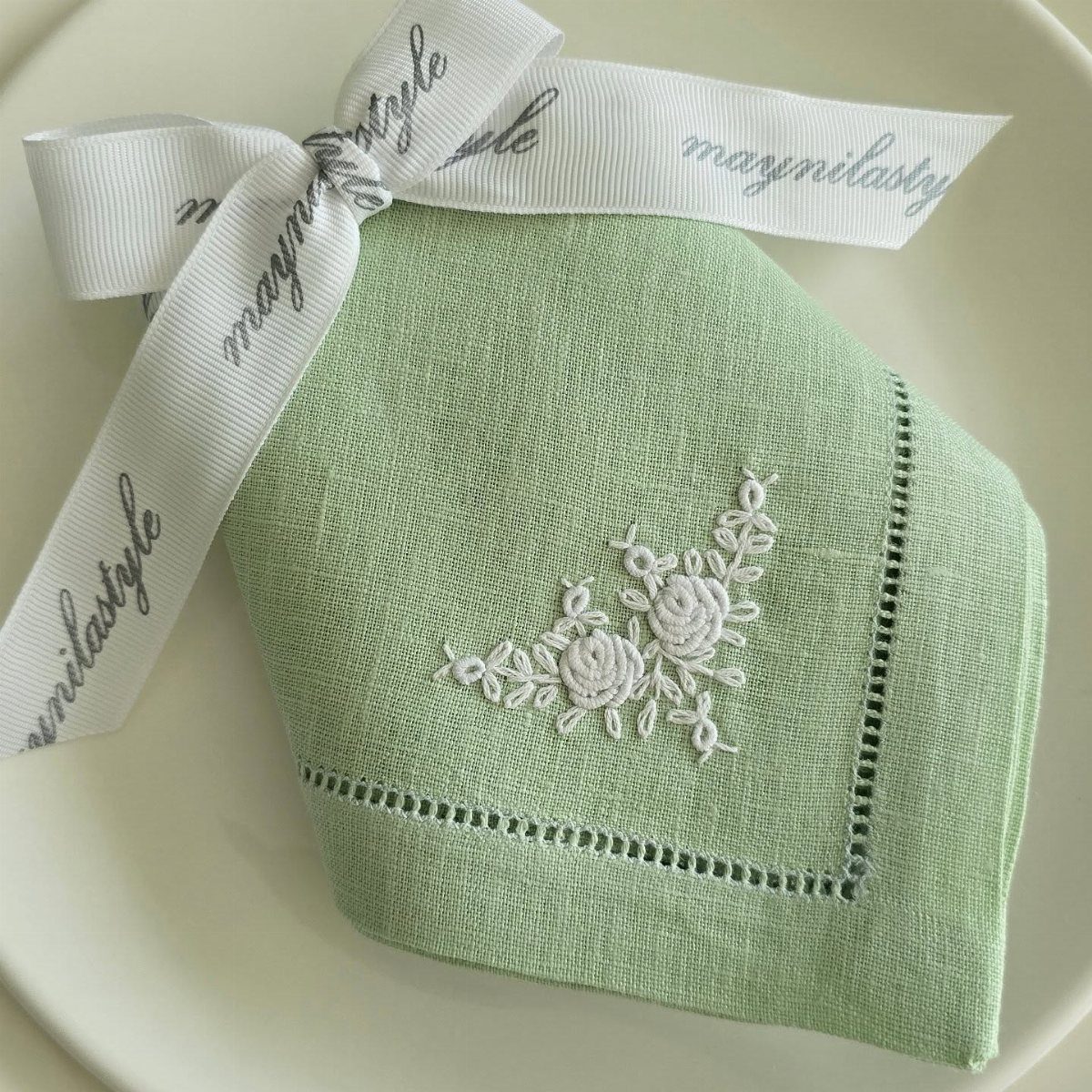 Green embroidered linen napkin tied with a white ribbon on a white plate