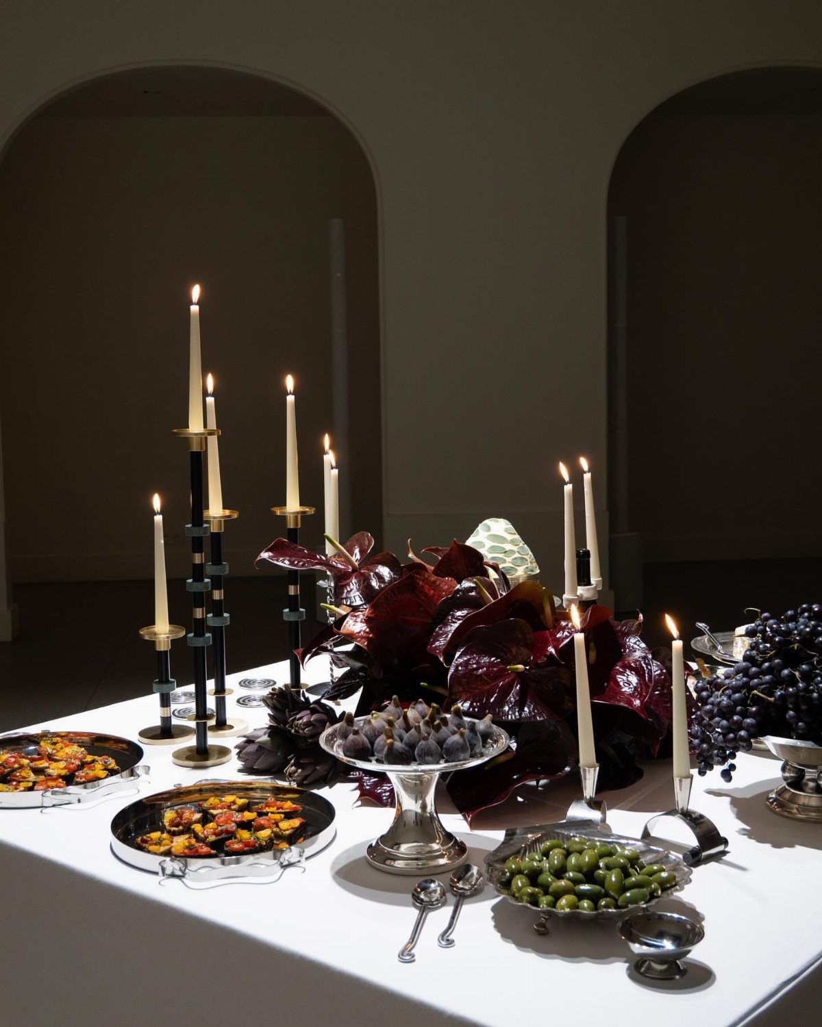 Table setting with dark red leaves, fruit bowls, and tall black candle holders.