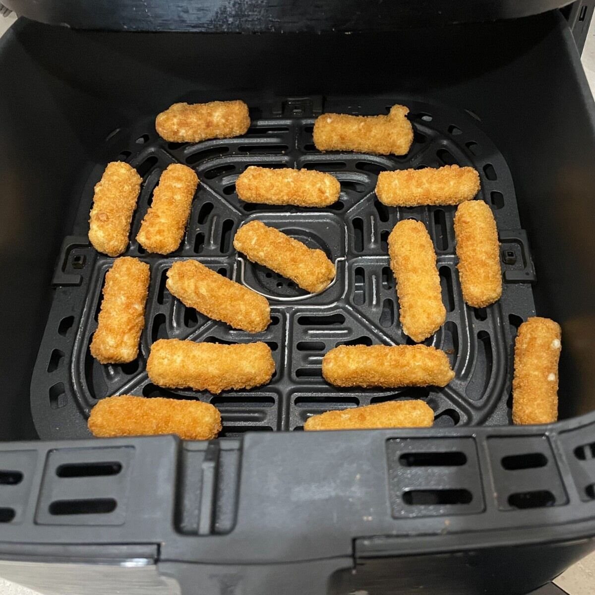Breaded mozzarella sticks cooking inside a black air fryer basket.