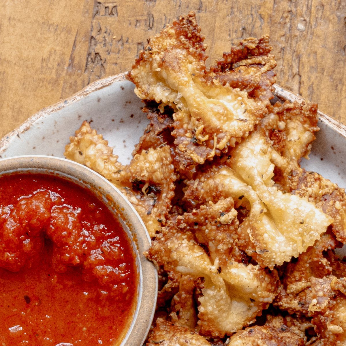 Fried farfalle pasta chips in a bowl with a side of red marinara sauce.
