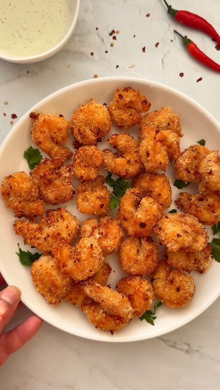 Breaded fried shrimp on a white plate with dipping sauce and red chilies.