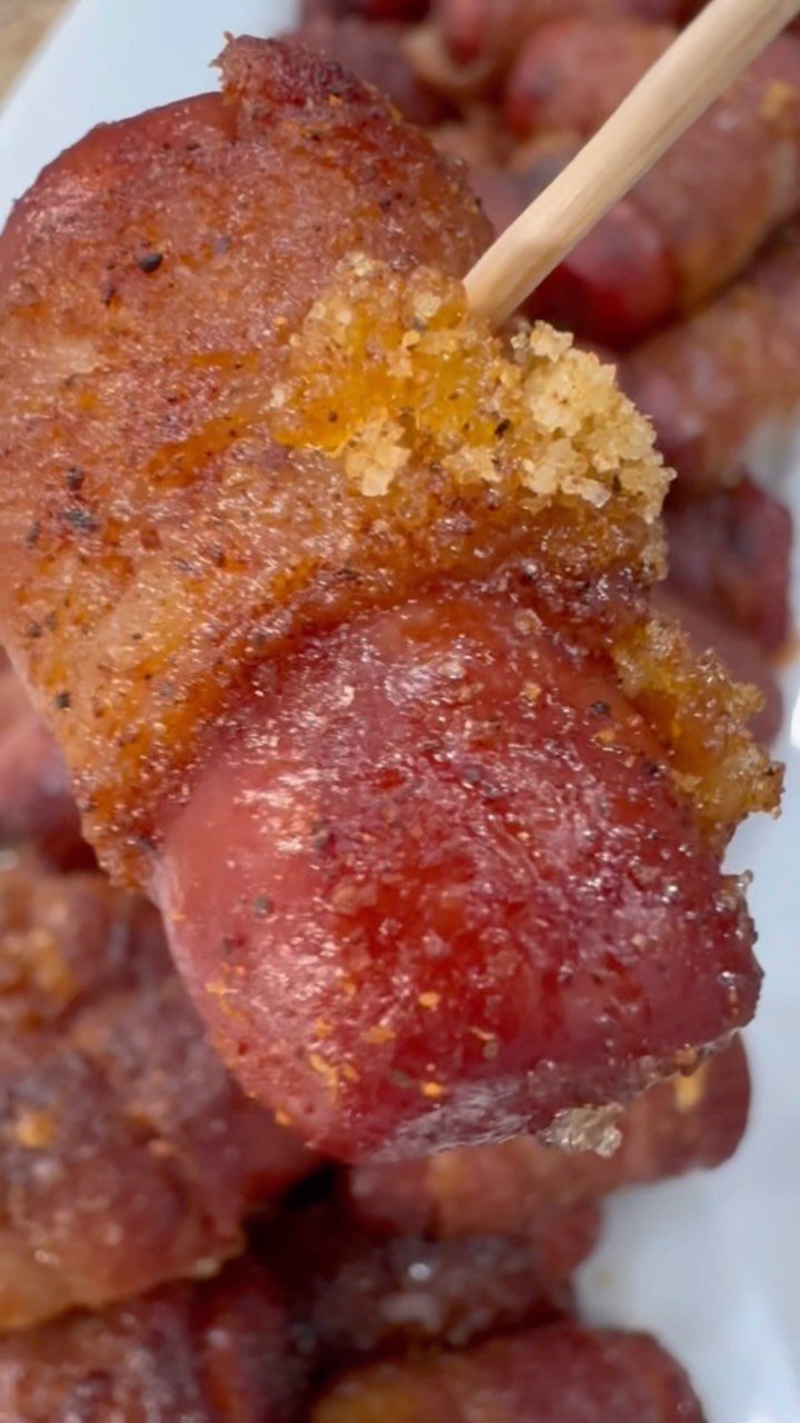 Bacon wrapped cocktail sausage on a toothpick with a brown glazed finish.