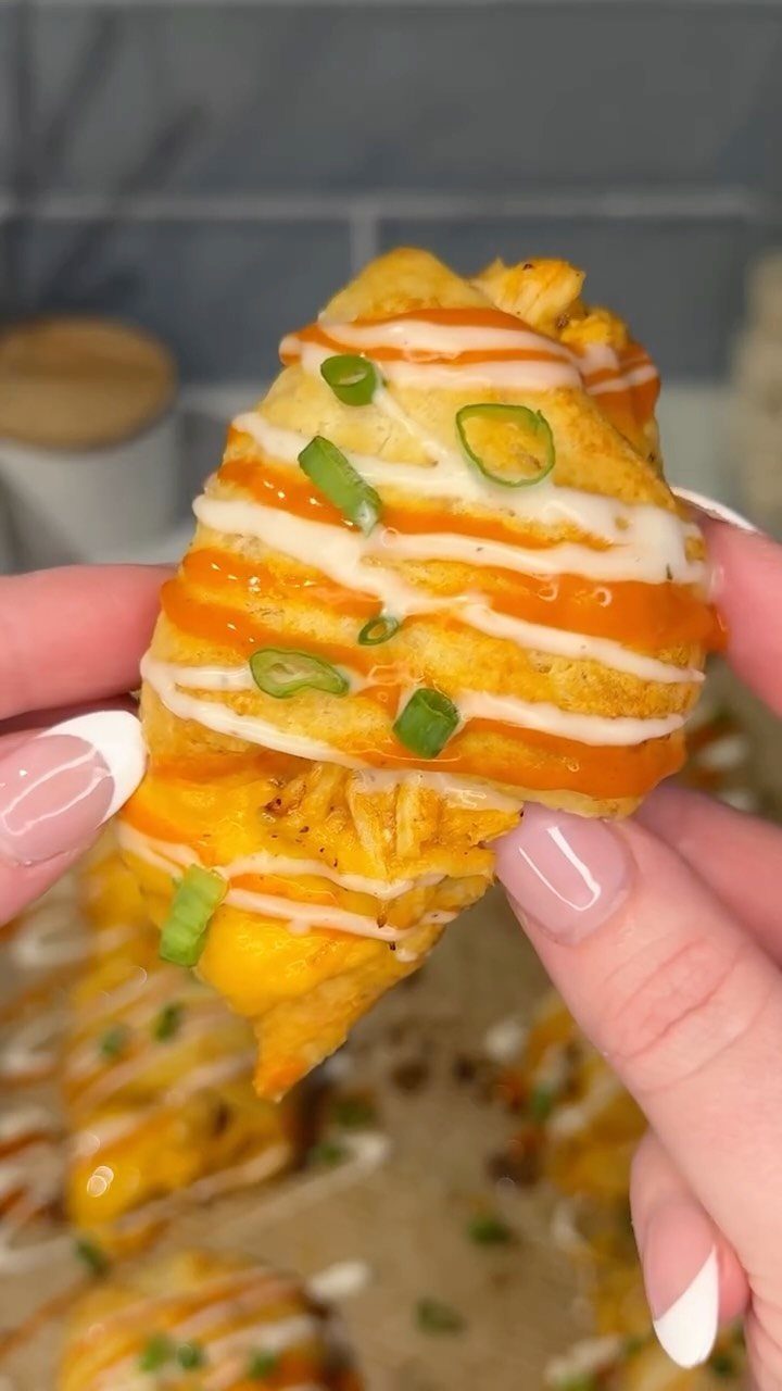 Buffalo chicken crescent roll with orange sauce and green onions held by hand.