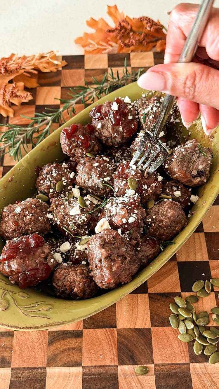 Glazed cranberry meatballs with pumpkin seeds in a green dish on wooden board.