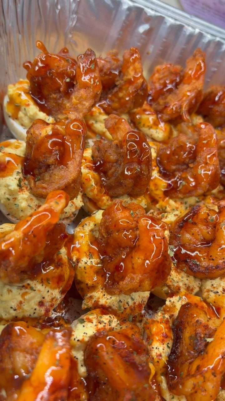 Deviled eggs topped with glazed fried shrimp in a silver foil tray