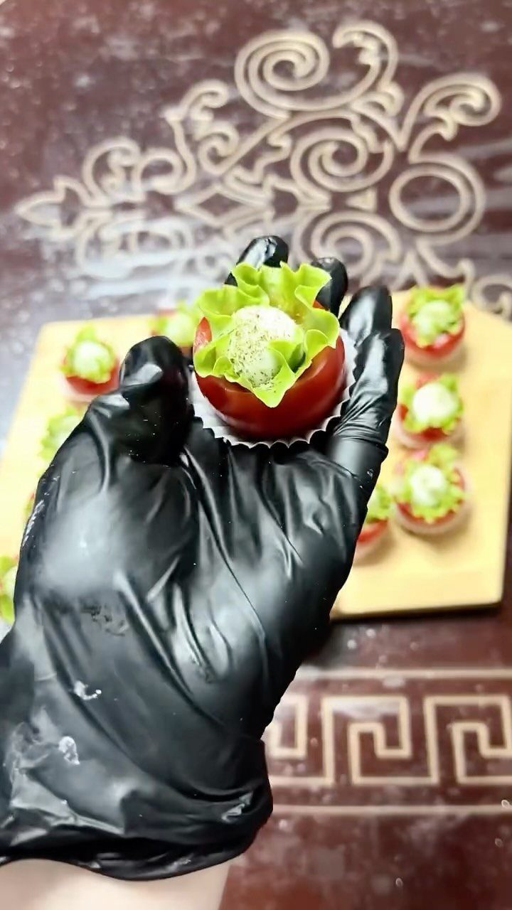Stuffed cherry tomato with white cheese and green garnish held in black glove
