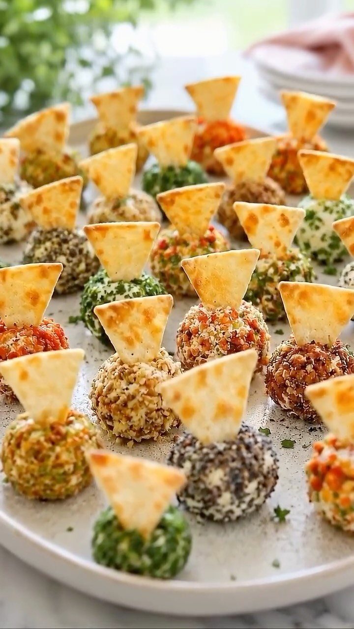 Assorted mini cheese balls with different coatings and triangular crackers on a platter