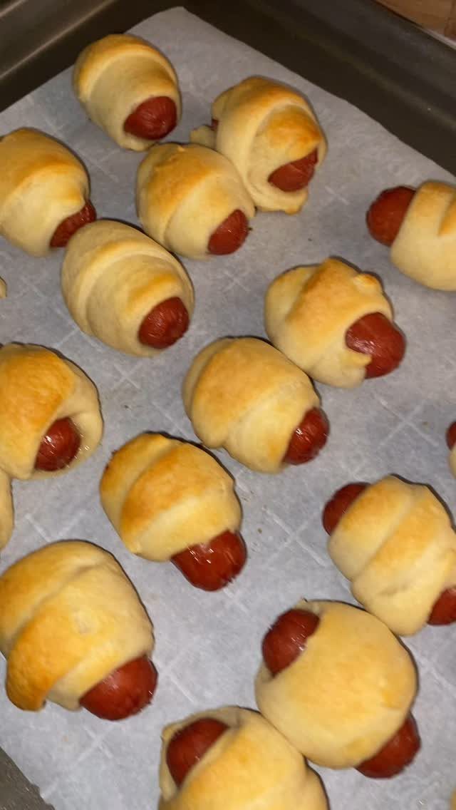 Mini sausages wrapped in golden pastry dough on a parchment-lined baking tray.