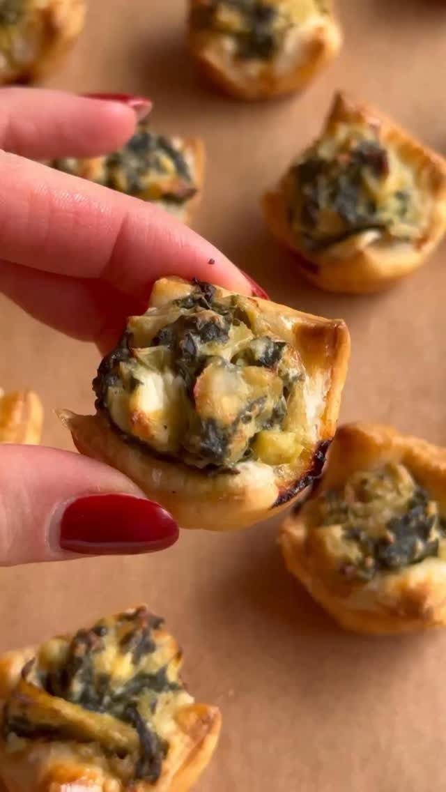 Spinach puff pastry bites held by a hand with red nail polish.