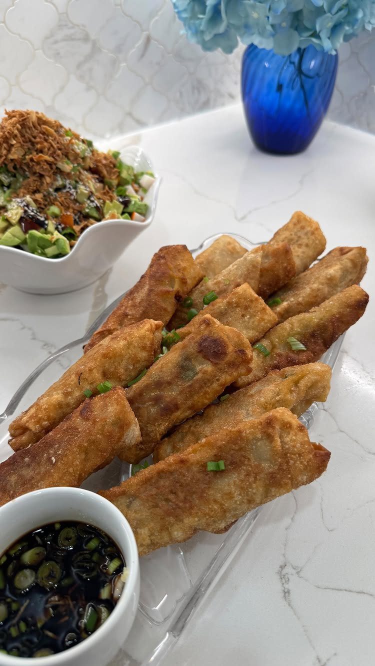 Fried egg rolls on a glass platter with dipping sauce and side salad.