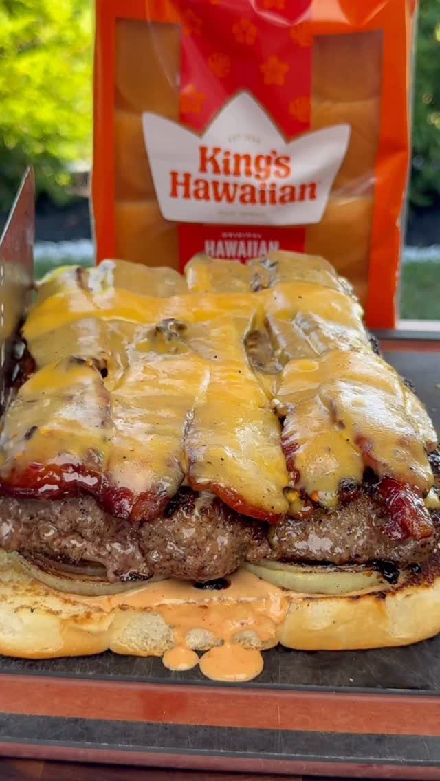 Bacon cheeseburgers with melted cheese on Hawaiian buns resting on a grill.
