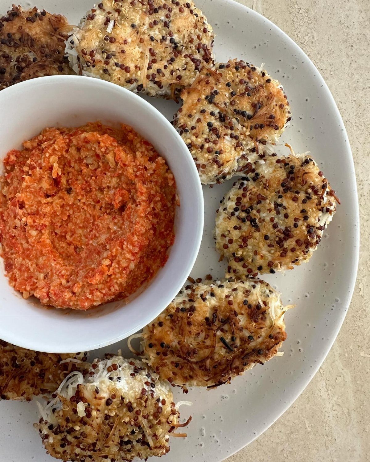 Quinoa chicken nuggets on a white plate with a bowl of red dipping sauce.