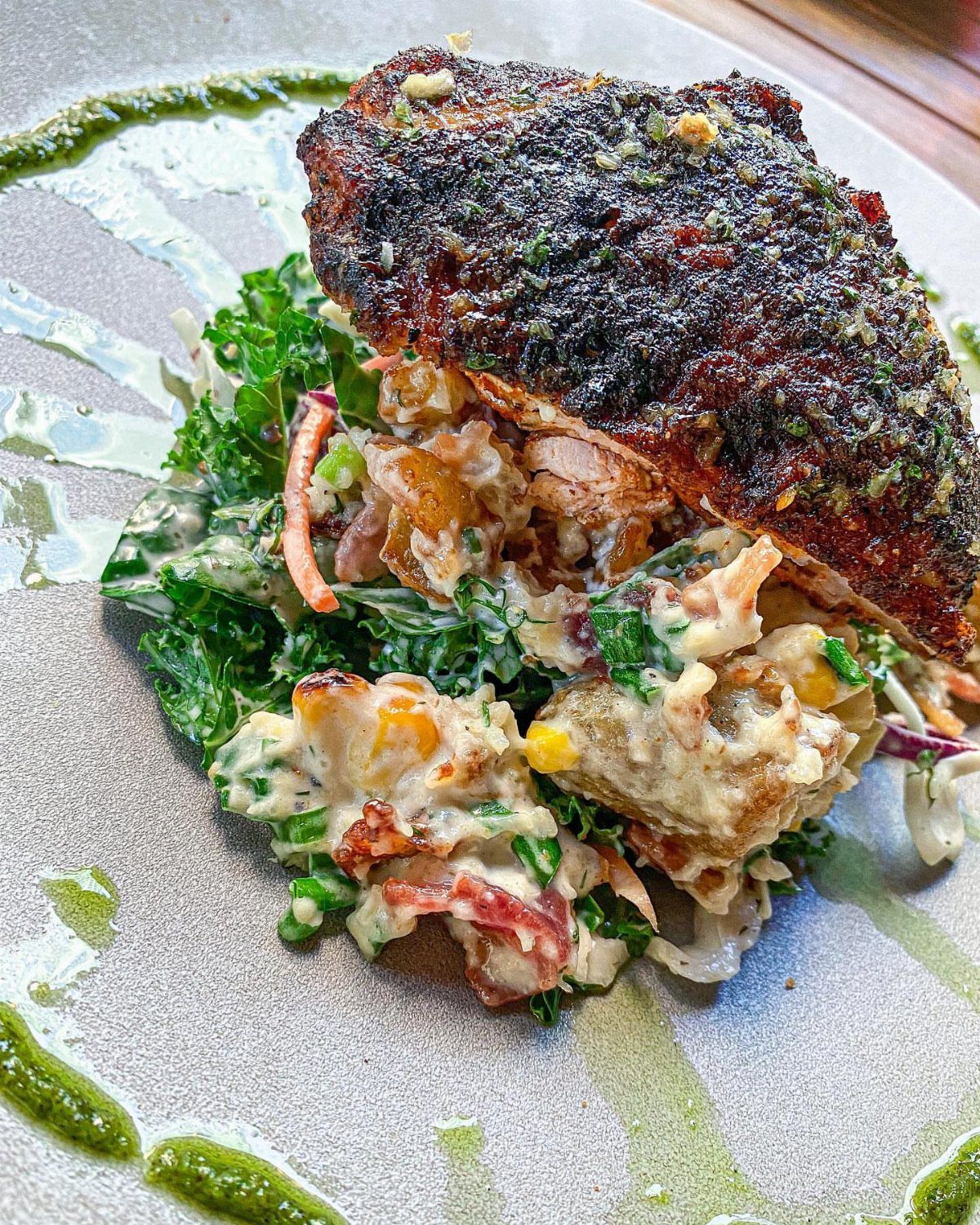 Blackened chicken breast served over a creamy kale and vegetable salad on a plate.