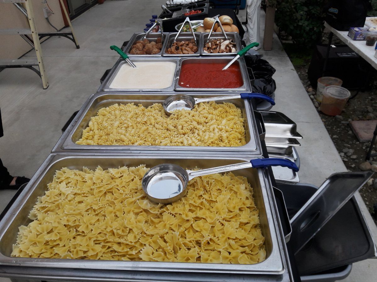 Buffet line with farfalle pasta, red tomato sauce, and various meat dishes.