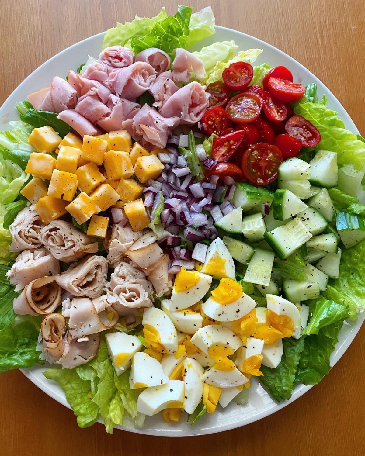 Cobb salad with ham, turkey, cheese, eggs, and vegetables on a white plate.